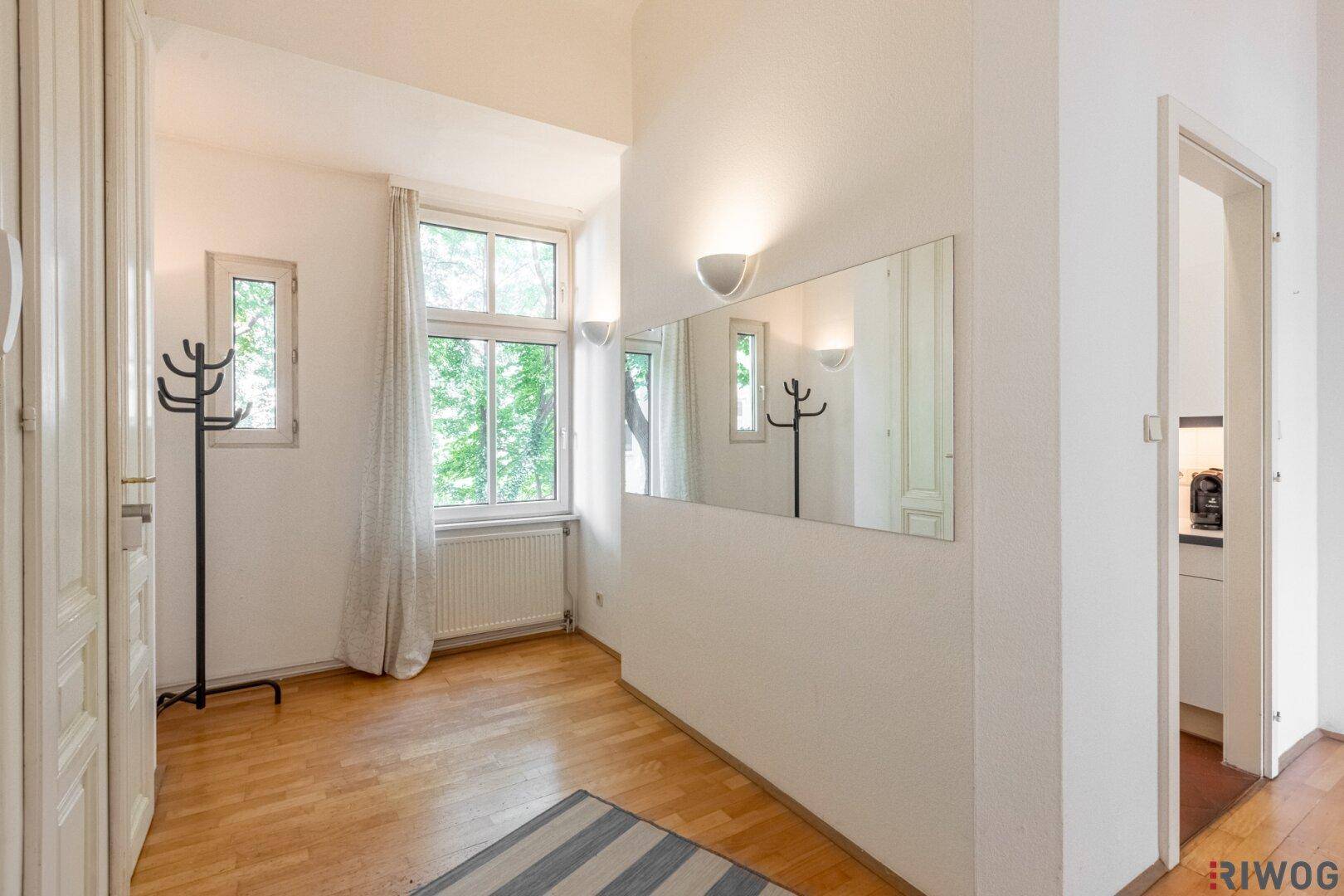 Heller Flur mit Parkettboden, großem Spiegel und Fenster mit Blick ins Grüne.
