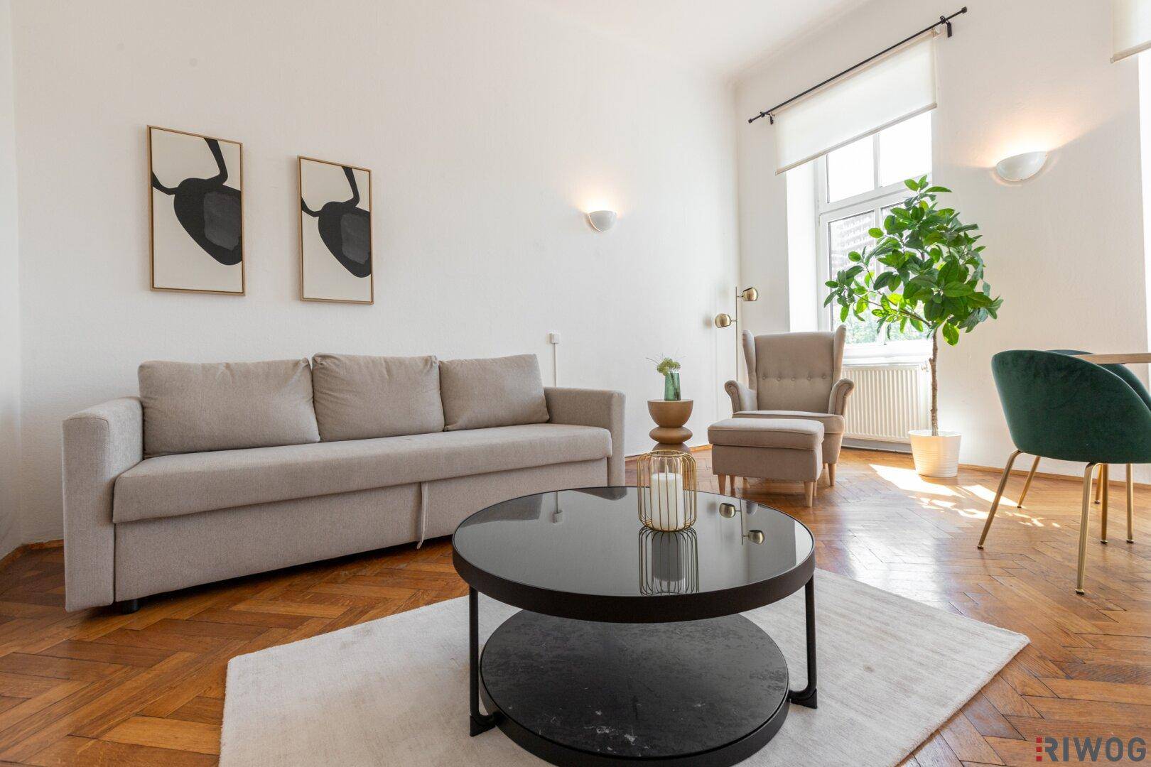 Helles Wohnzimmer mit beigem Sofa, dunklem Couchtisch und Blick durch große Fenster.