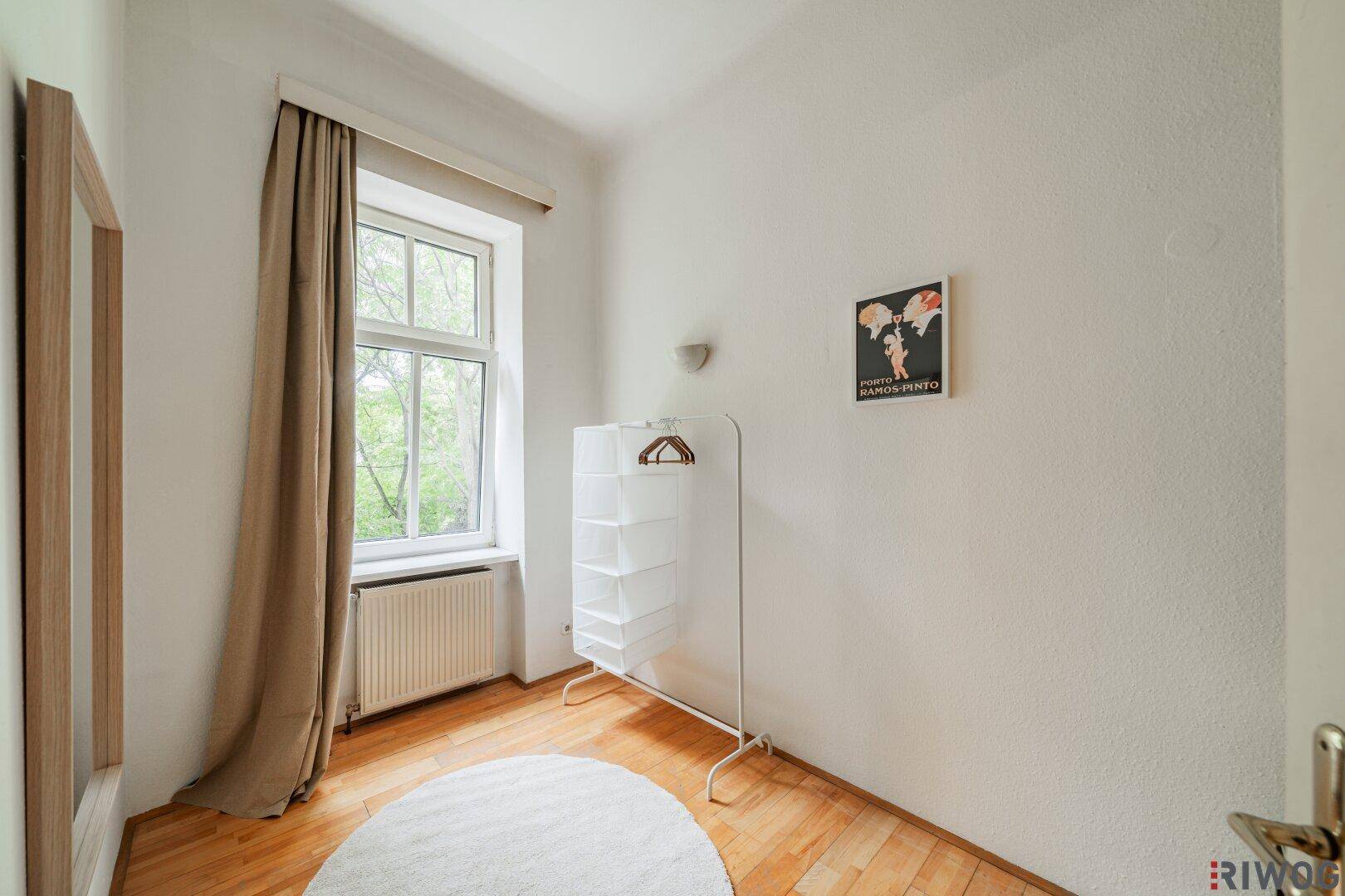 Helles Schlafzimmer mit Holzboden, Fenster und einem Kleiderständer.