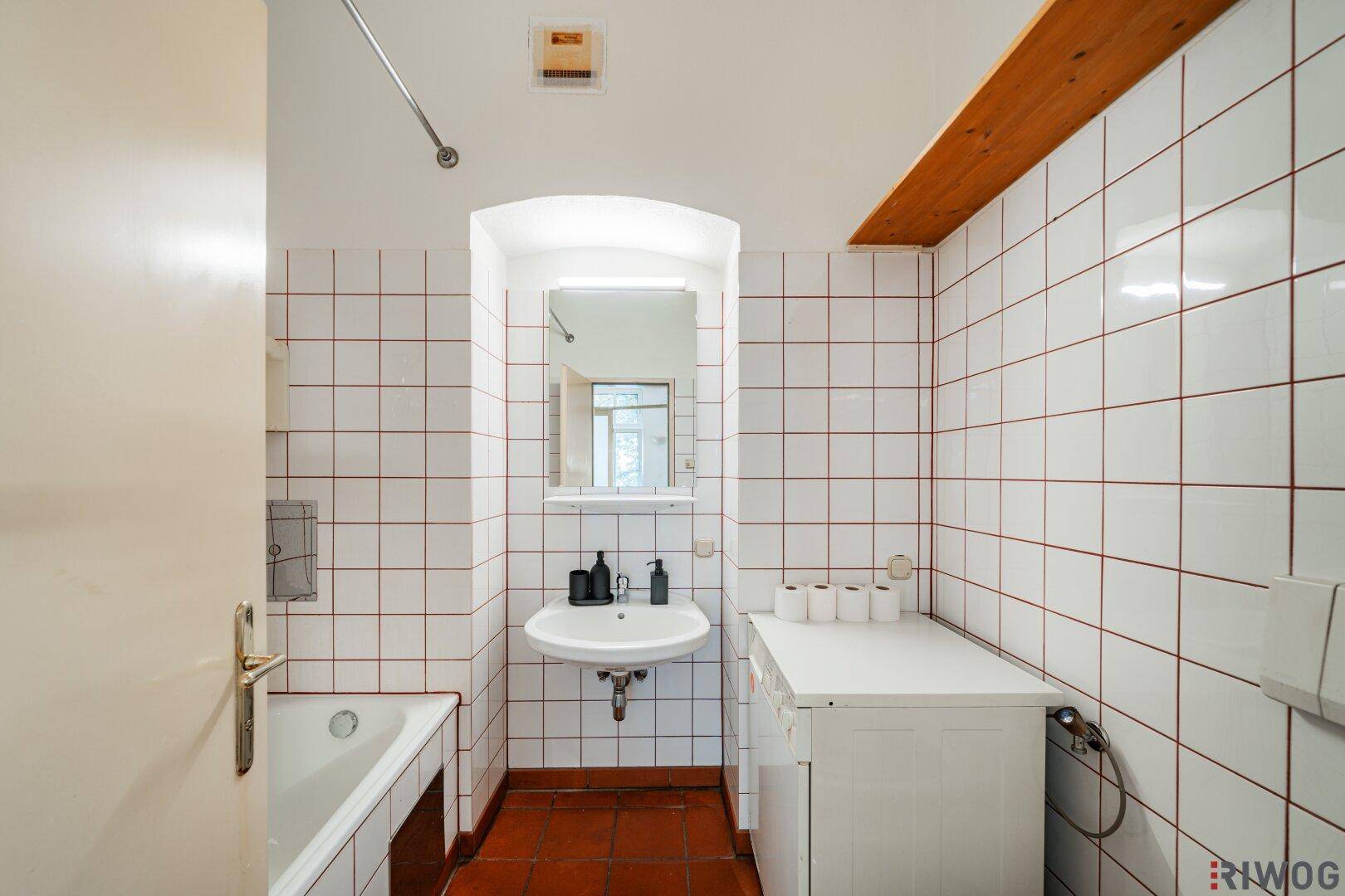 Badezimmer mit Badewanne, Waschbecken und Waschmaschine, gefliest in Weiß und Rotbraun.