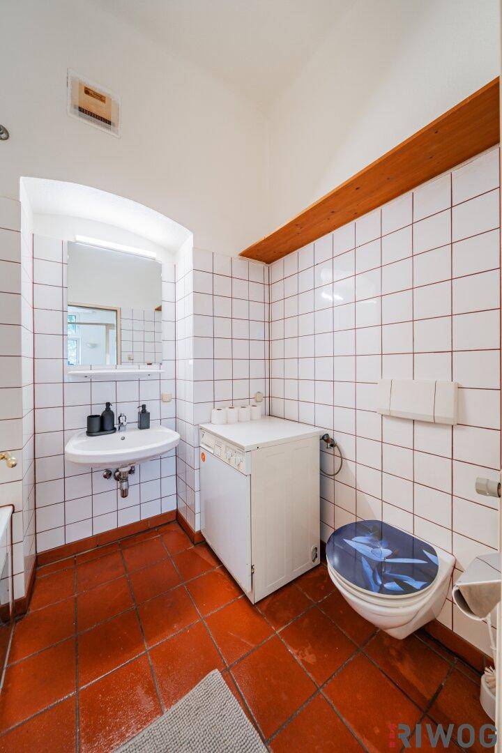Badezimmer mit Toilette, Waschbecken und Waschmaschine, gefliest mit roten Akzenten.