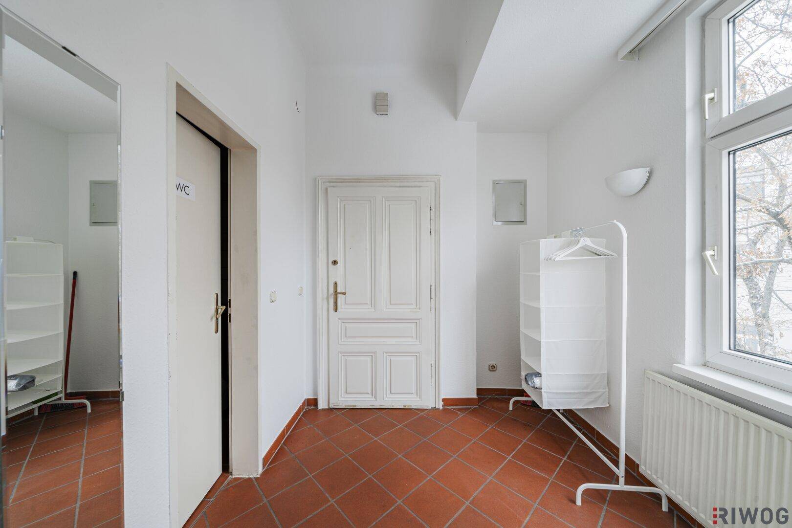 Eingangsbereich mit Terrakottafliesen, großem Spiegel und Zugang zu weiteren Räumen, inklusive WC.