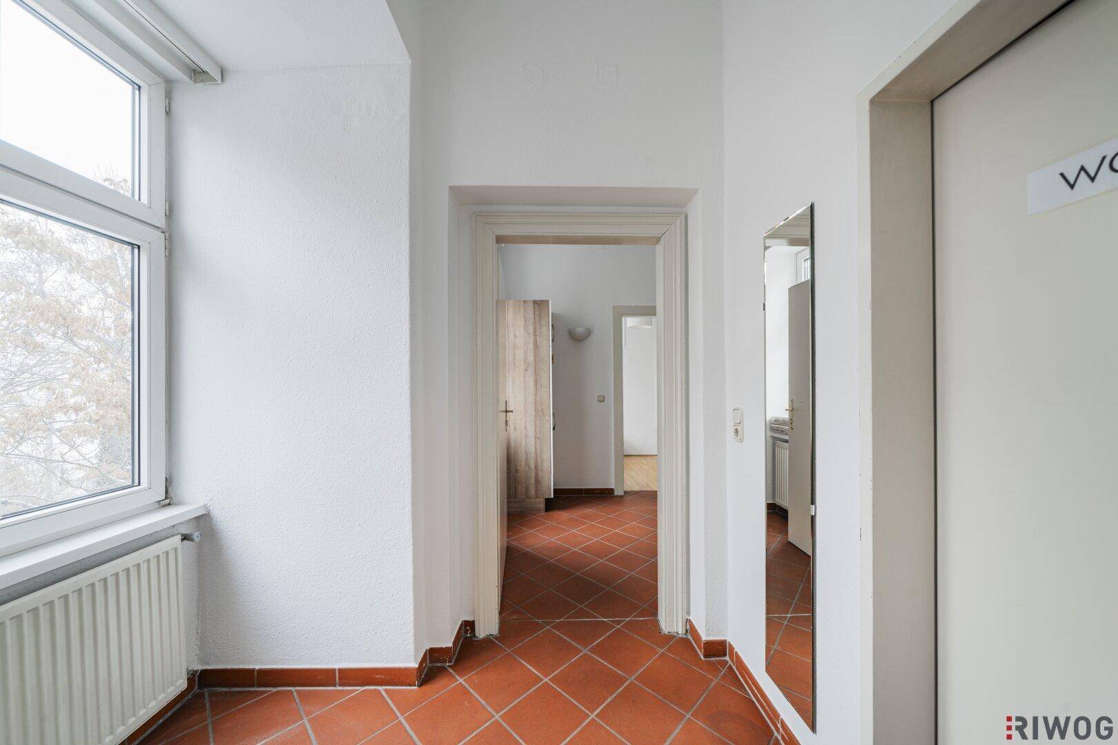 Heller Flur mit Terrakottafliesen, Fenster und Blick in angrenzende Zimmer, funktional eingerichtet.