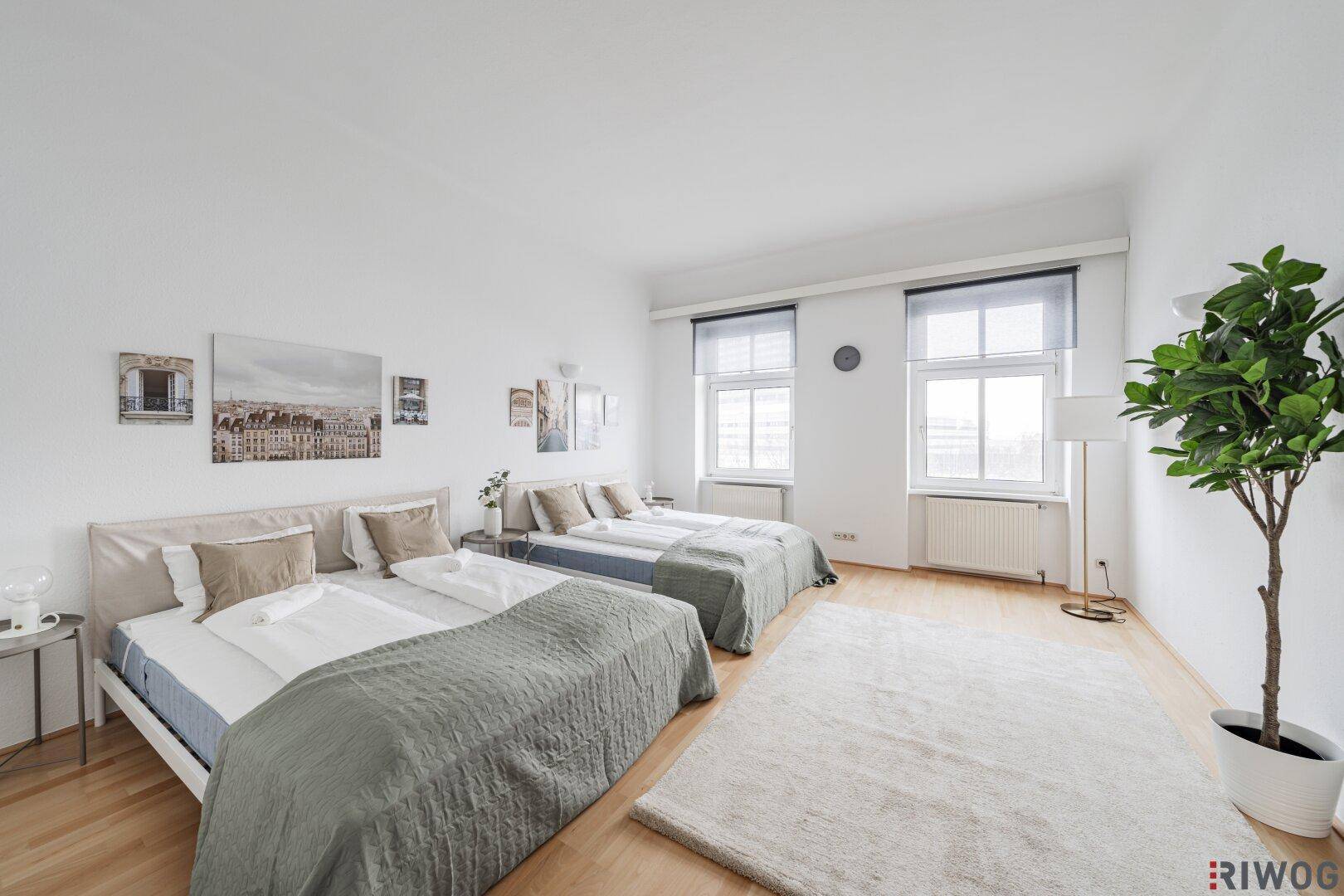 Helles Schlafzimmer mit zwei Betten, Holzboden und großen Fenstern, ideal für Gäste.