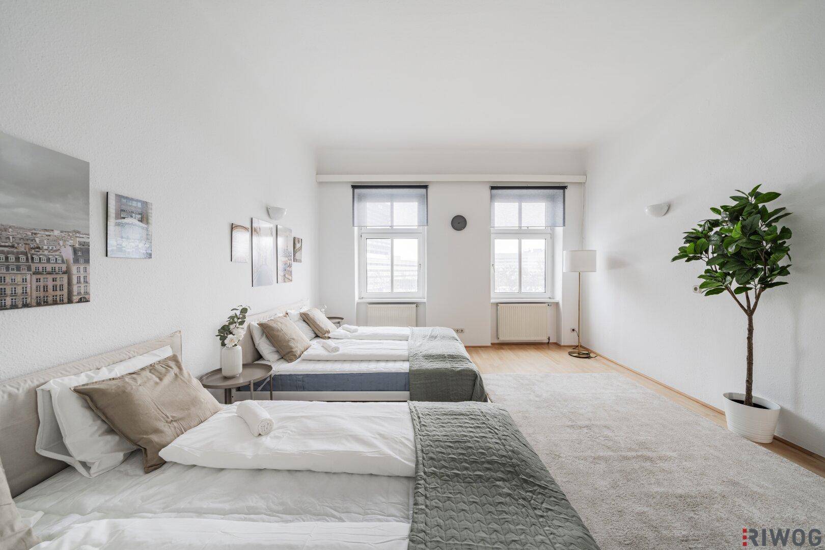 Lichtdurchflutetes Schlafzimmer mit zwei Einzelbetten, Holzboden und schlichter Dekoration.