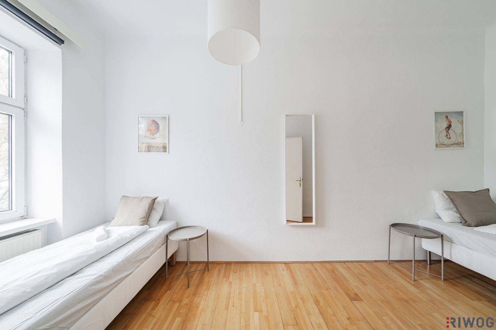 Helles Schlafzimmer mit zwei Einzelbetten, Holzboden und natürlichem Lichteinfall durch das Fenster.