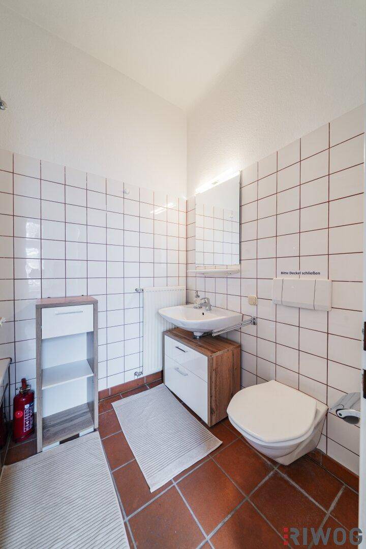 Badezimmer mit weißen Wandfliesen, Terrakotta-Bodenfliesen, Waschbecken und WC, funktional gestaltet.