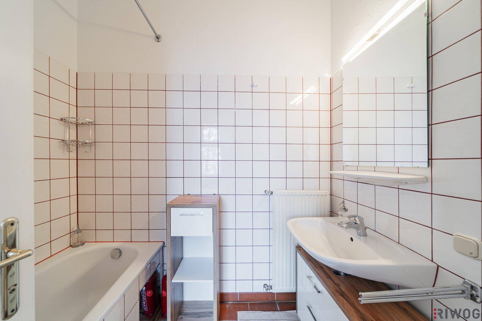 Helles Badezimmer mit Badewanne, Waschbecken und weißen Fliesen, praktisch und sauber.