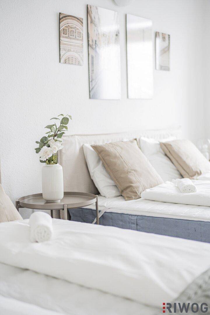 Nahaufnahme eines Bettes mit Nachttisch und frischen Blumen, schafft eine gemütliche Atmosphäre.