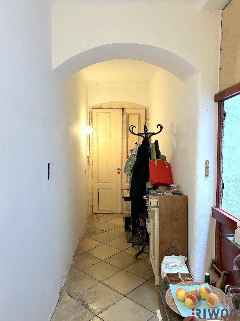 Langer Flur mit Bogen, Fliesenboden und Garderobe.