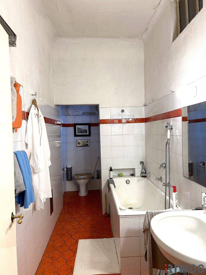 Badezimmer mit Badewanne, Fliesenboden und Renovierungsbedarf.