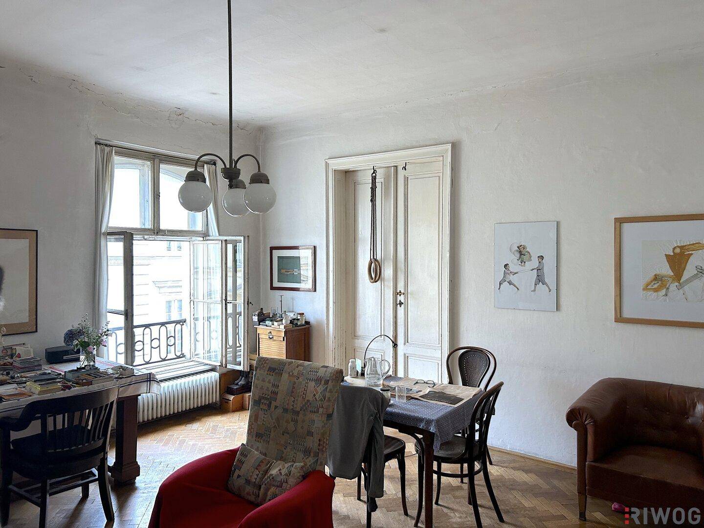 Helles Wohnzimmer mit Parkettboden, großem Fenster und Blick auf die Straße.