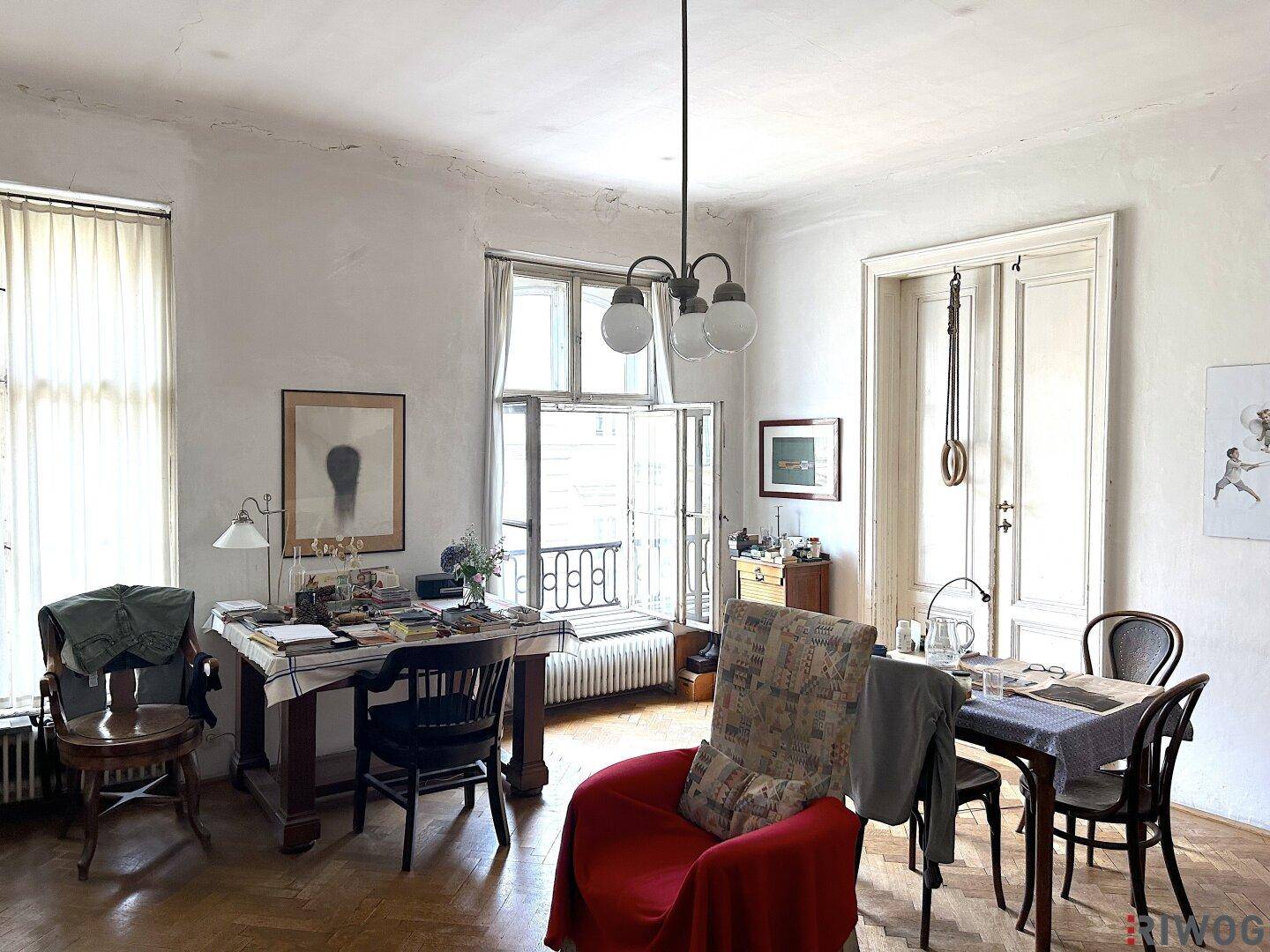 Wohnzimmer mit Parkettboden, großem Fenster und traditioneller Einrichtung.