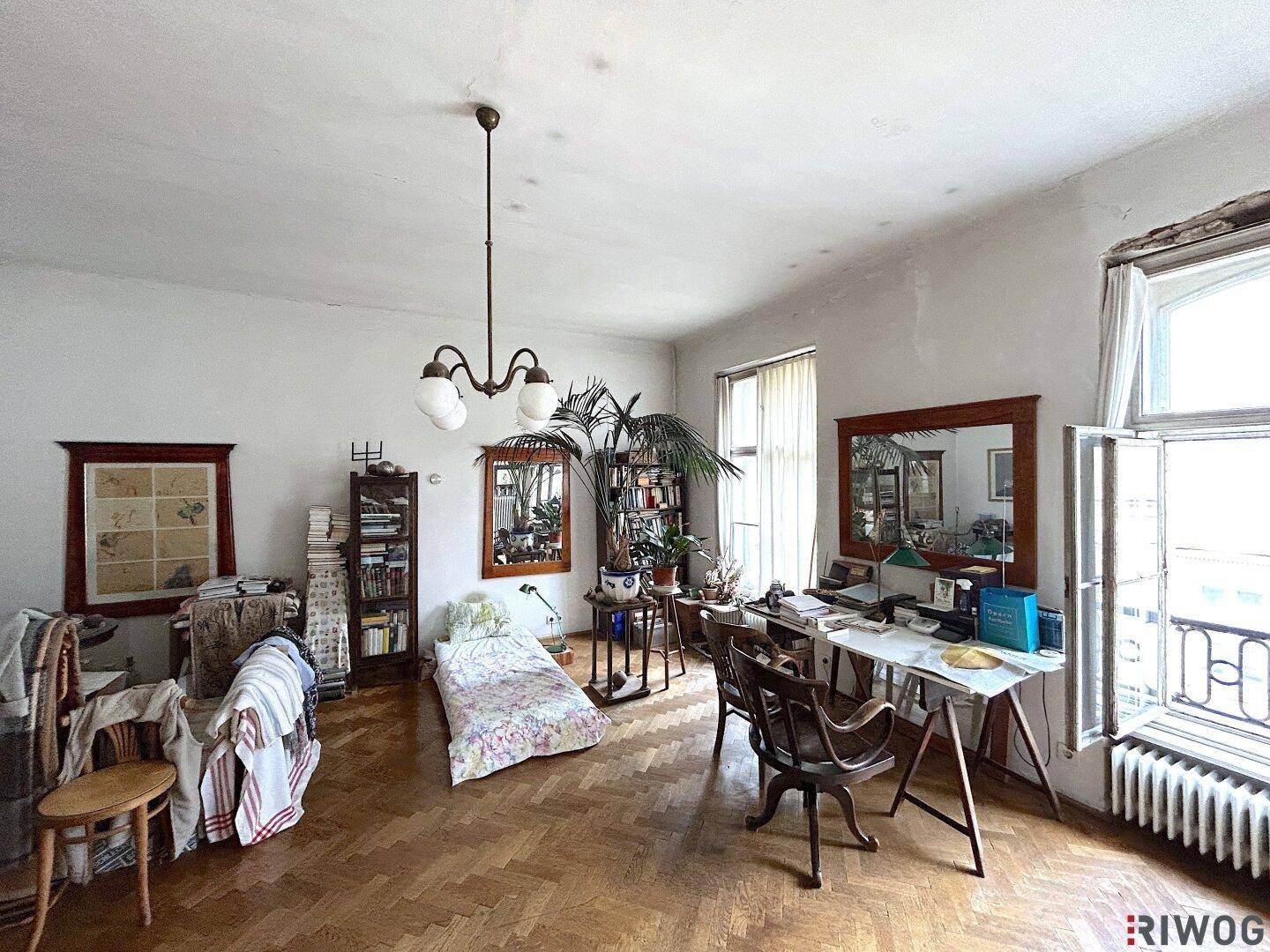 Geräumiges Wohnzimmer mit Fischgrätparkett, hohen Decken und Renovierungsbedarf.
