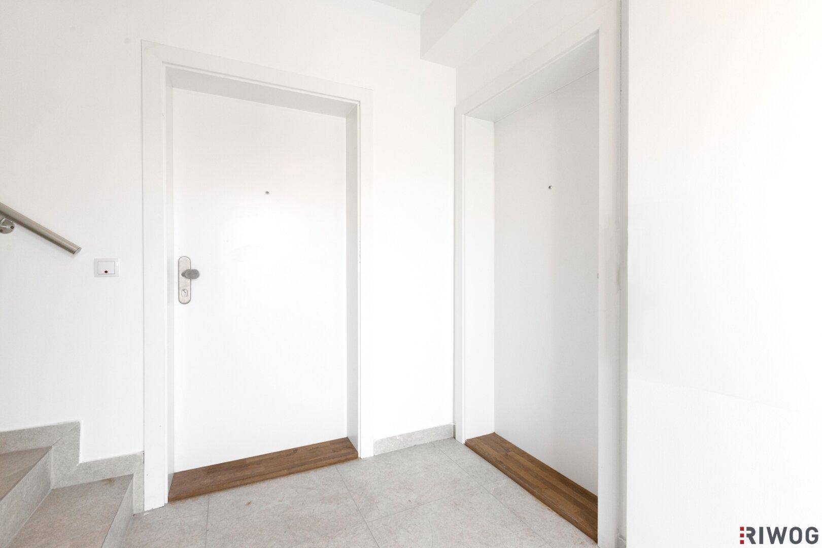 Zwei weiße Wohnungstüren in einem hellen Flur mit grauen Fliesen und einem Treppengeländer.