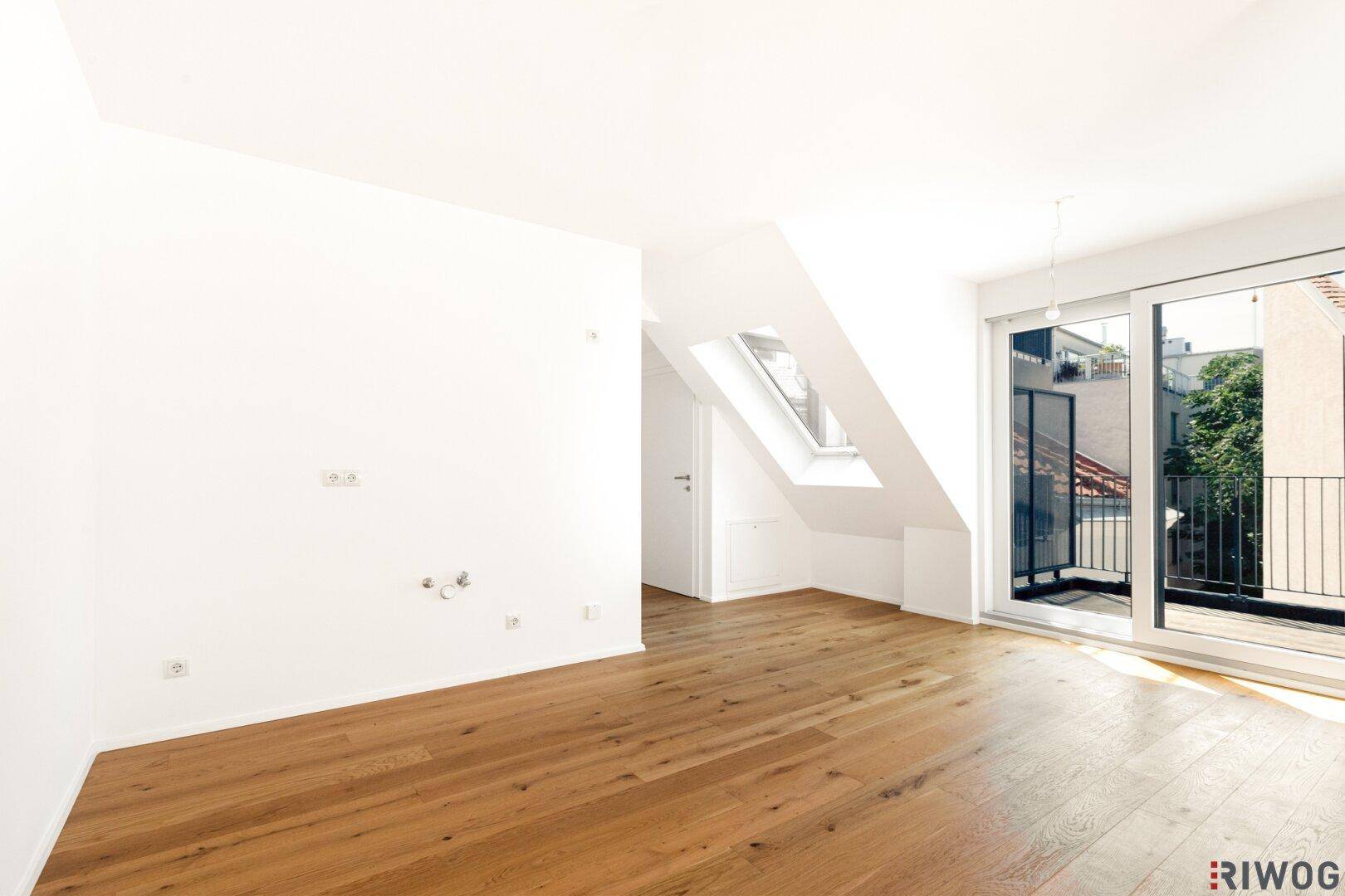 Heller, leerer Raum im Dachgeschoss mit Holzboden und Zugang zum Balkon.