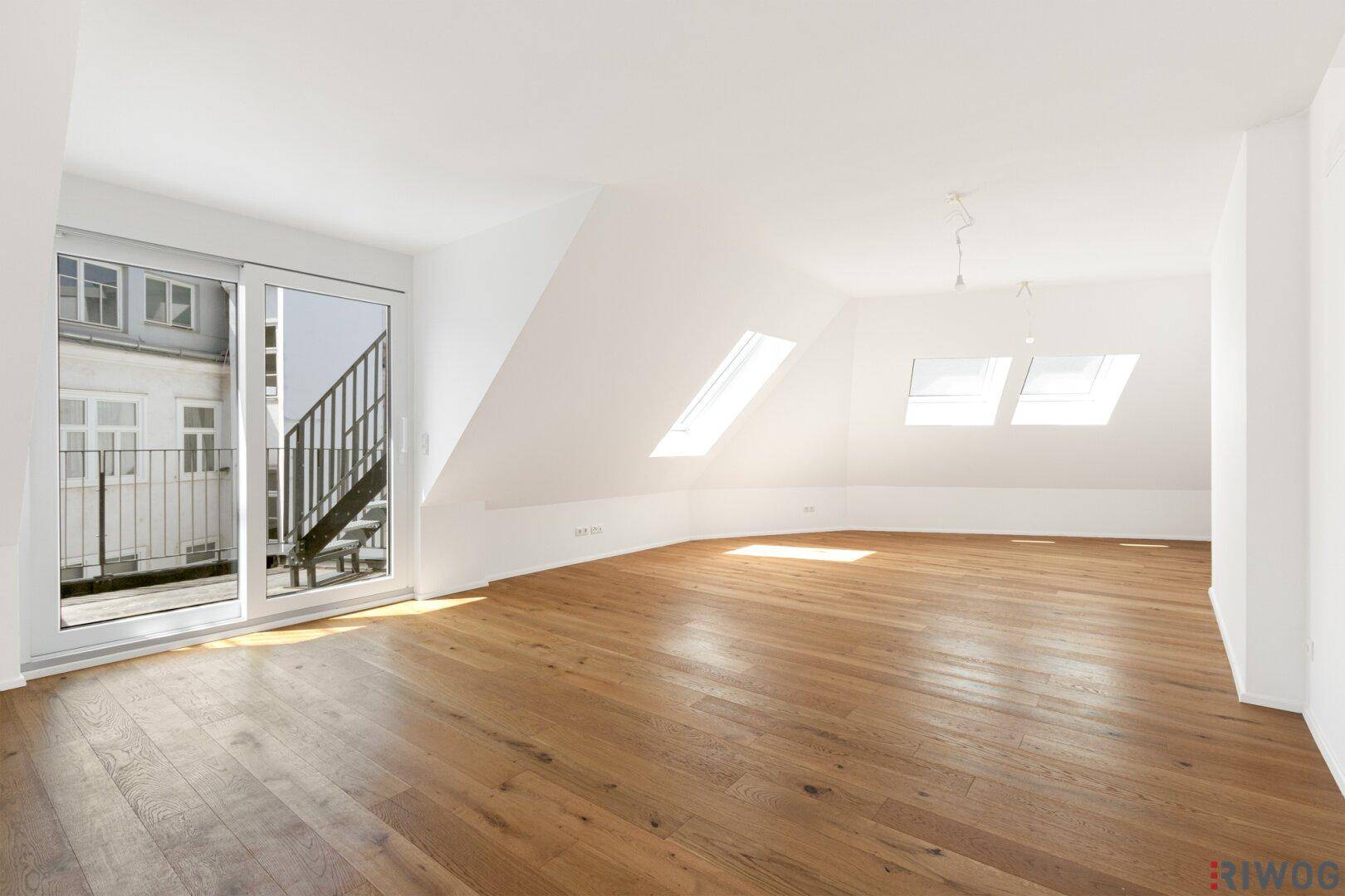 Lichtdurchfluteter Dachgeschossraum mit Holzboden, großen Fenstern und Dachschrägen.