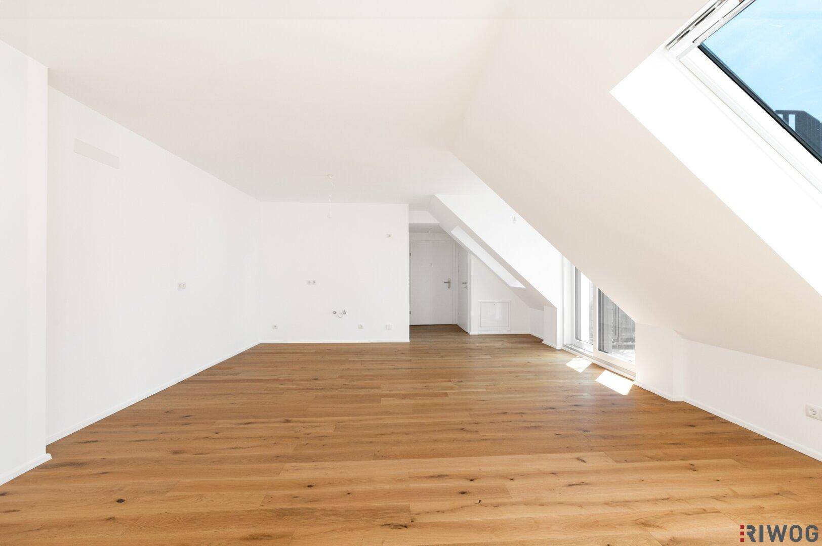 Moderner, heller Dachgeschossraum mit Holzboden und großen Fenstern.