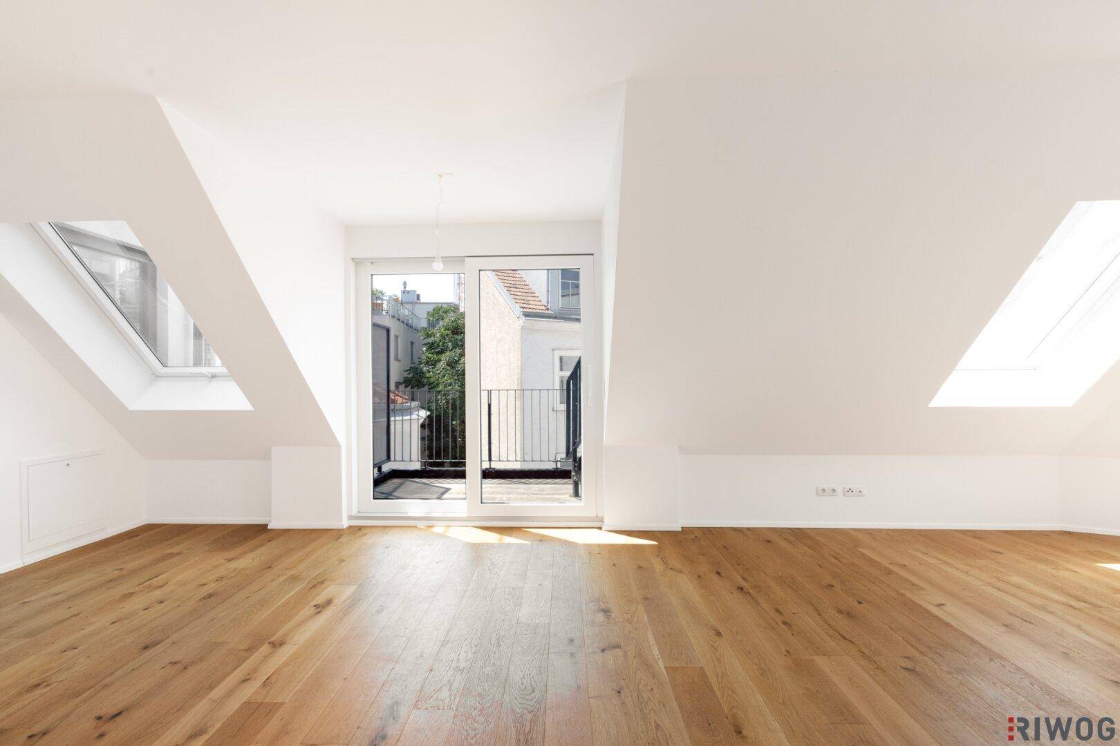 Geräumiger und heller Dachgeschossraum mit Holzboden und Zugang zu einem kleinen Balkon.
