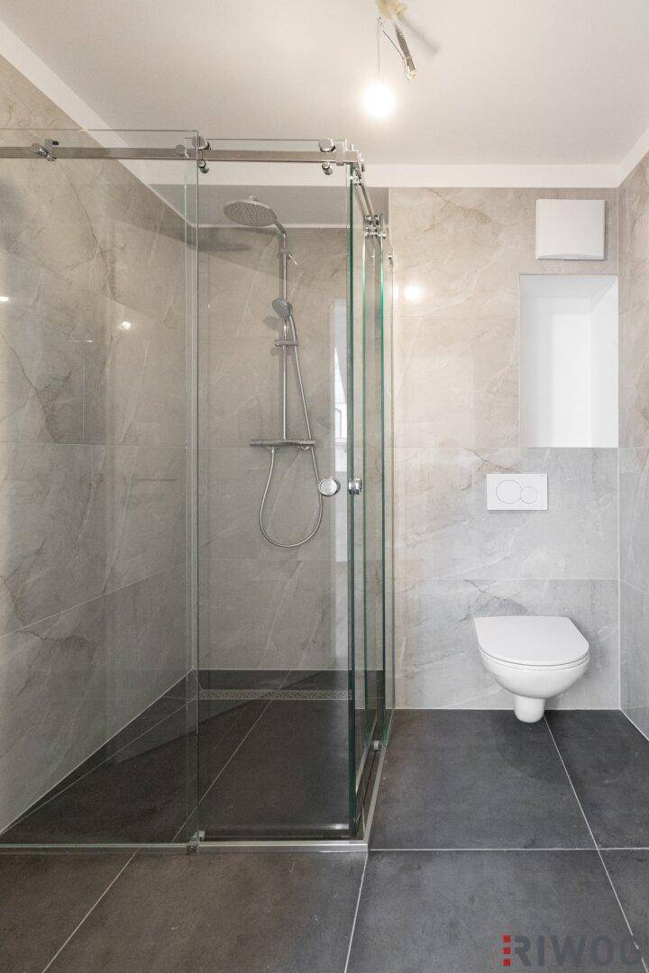 Modernes Badezimmer mit großer Duschkabine, Wand-WC und grauen Fliesen.