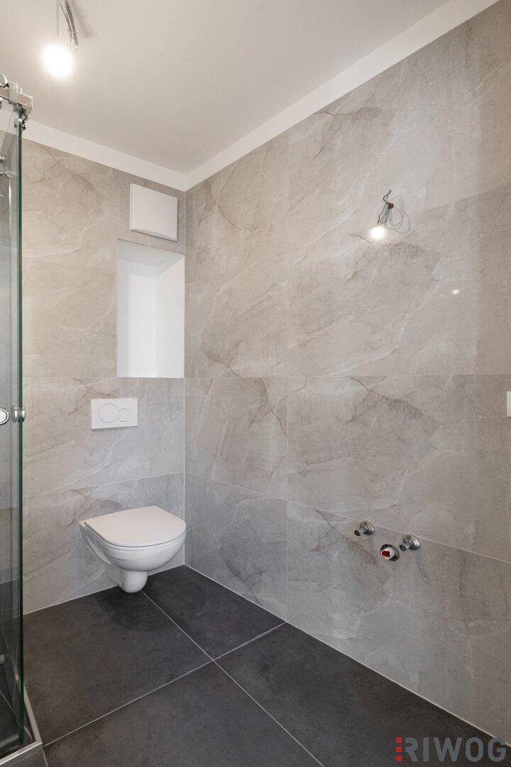 Helles Badezimmer mit moderner Duschkabine und Wand-WC, bereit für die Installation eines Waschbeckens.