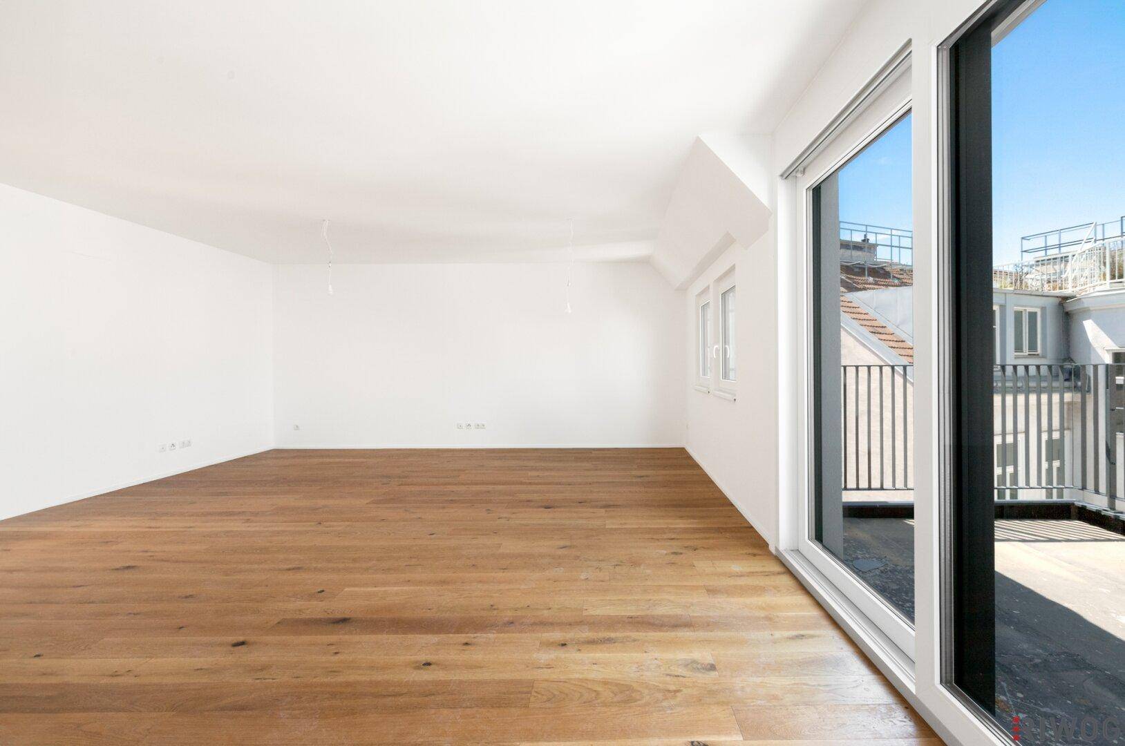 Lichtdurchfluteter Raum mit Holzboden und großen Fenstern, die viel Tageslicht hereinlassen.