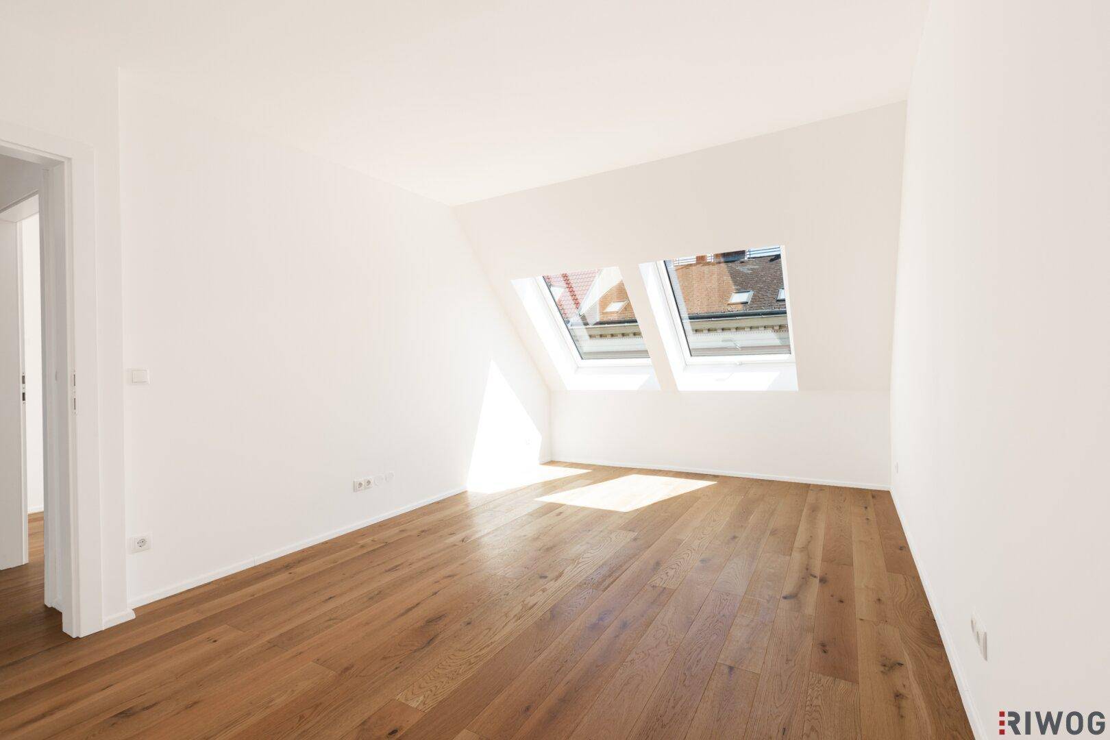 Helles Dachzimmer mit schrägen Wänden, Parkettboden und zwei Dachfenstern für viel Licht.