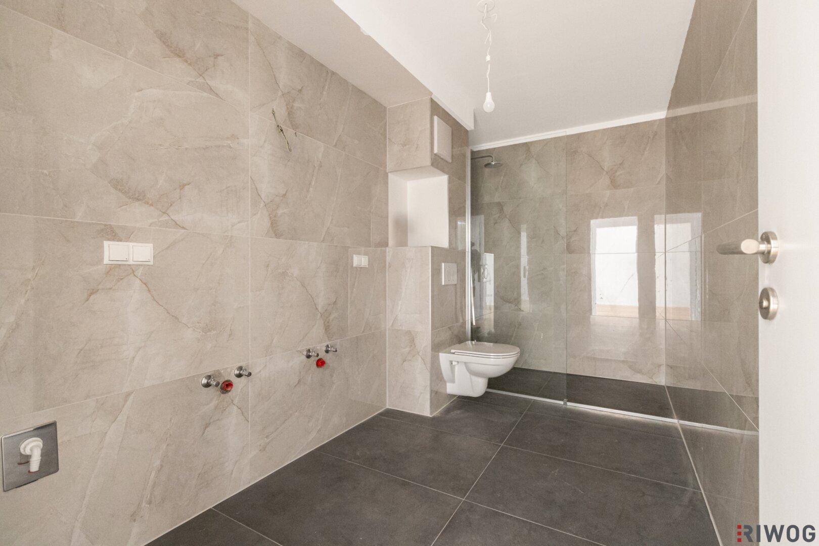 Modernes Badezimmer mit großformatigen grauen Fliesen, bodengleicher Dusche und Wand-WC.
