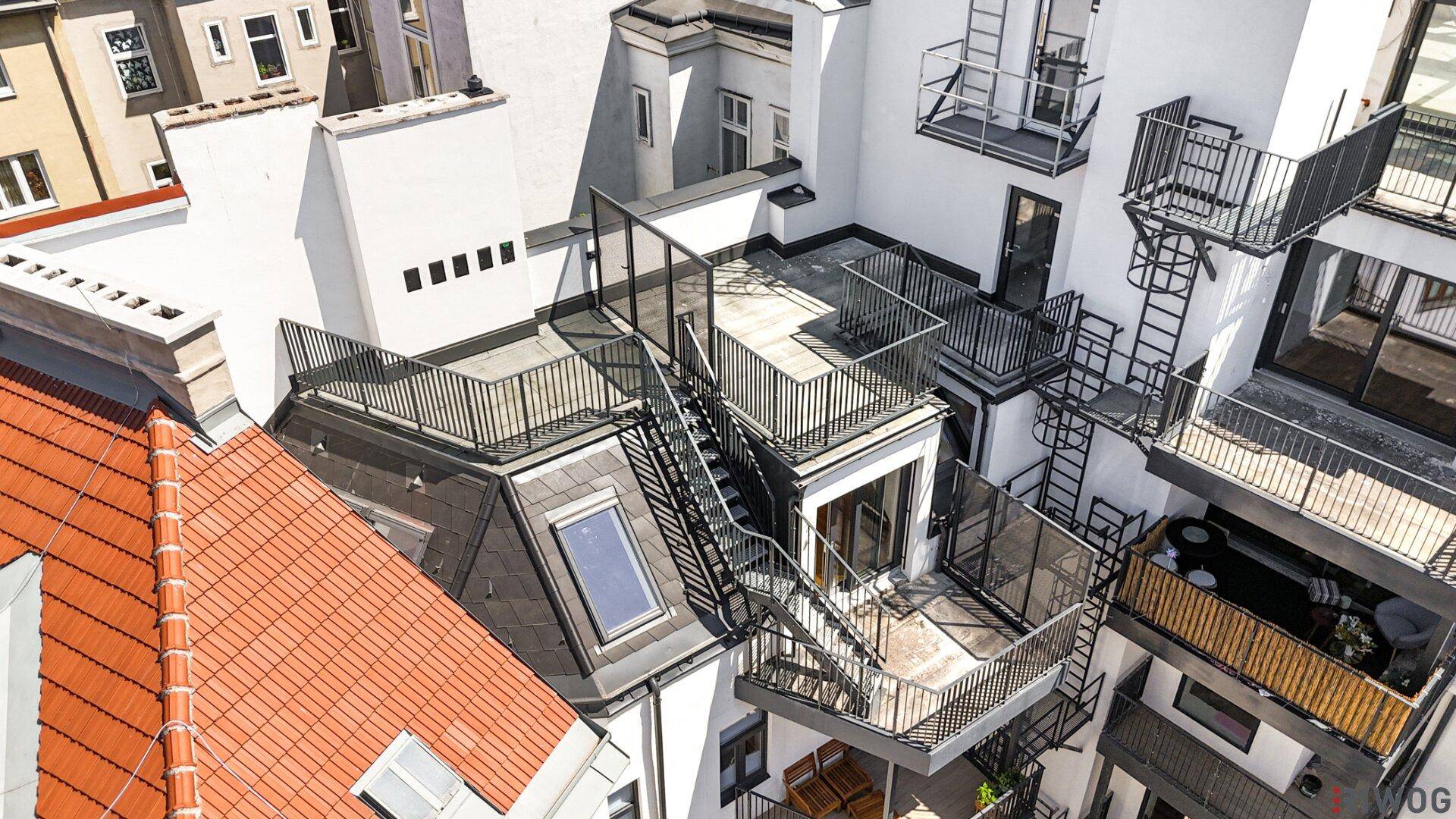 Luftaufnahme eines Gebäudes mit mehreren Dachterrassen, Balkonen und externen Treppen.