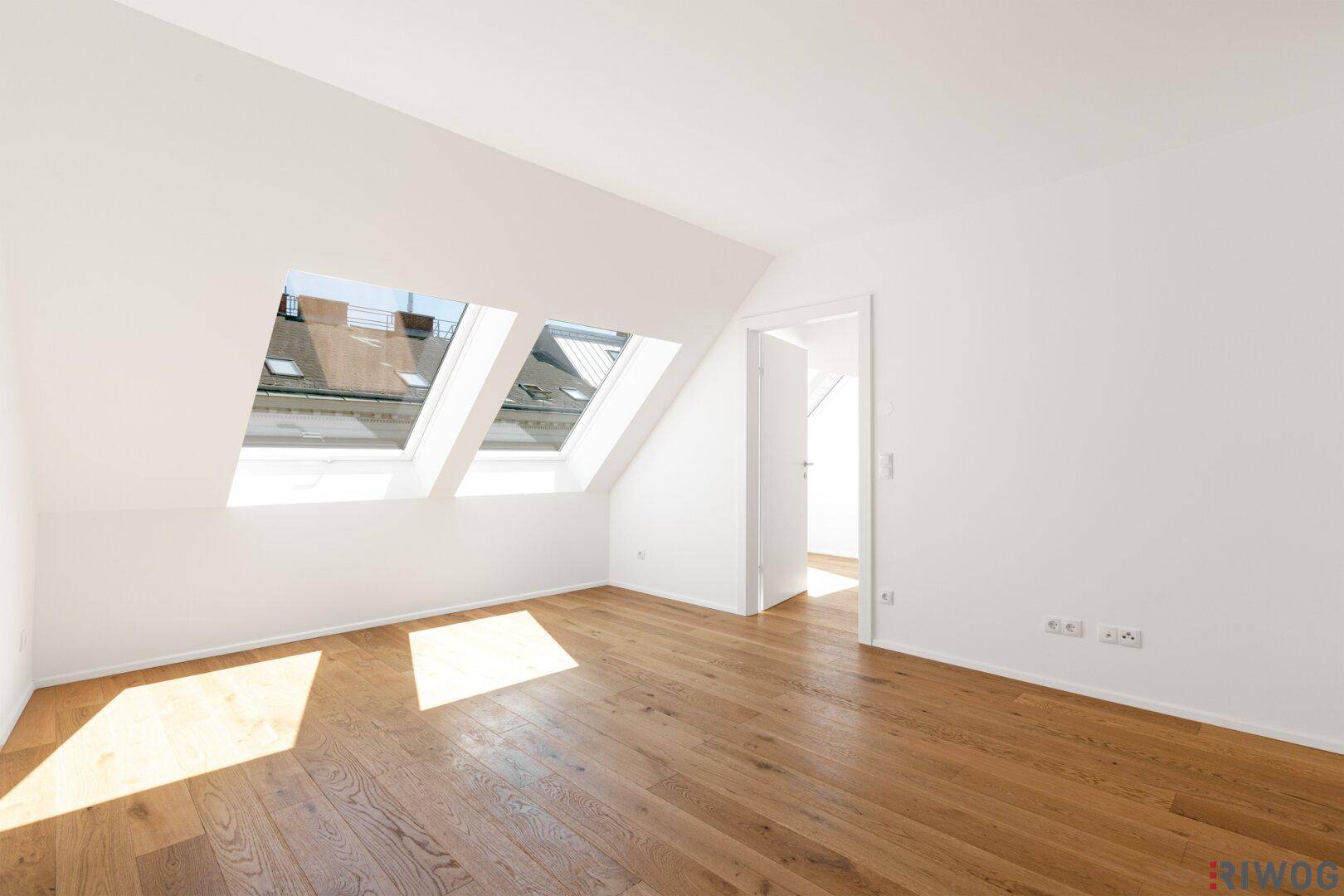 Geräumiger Dachgeschossraum mit viel Tageslicht durch zwei große Dachfenster und elegantem Holzboden.