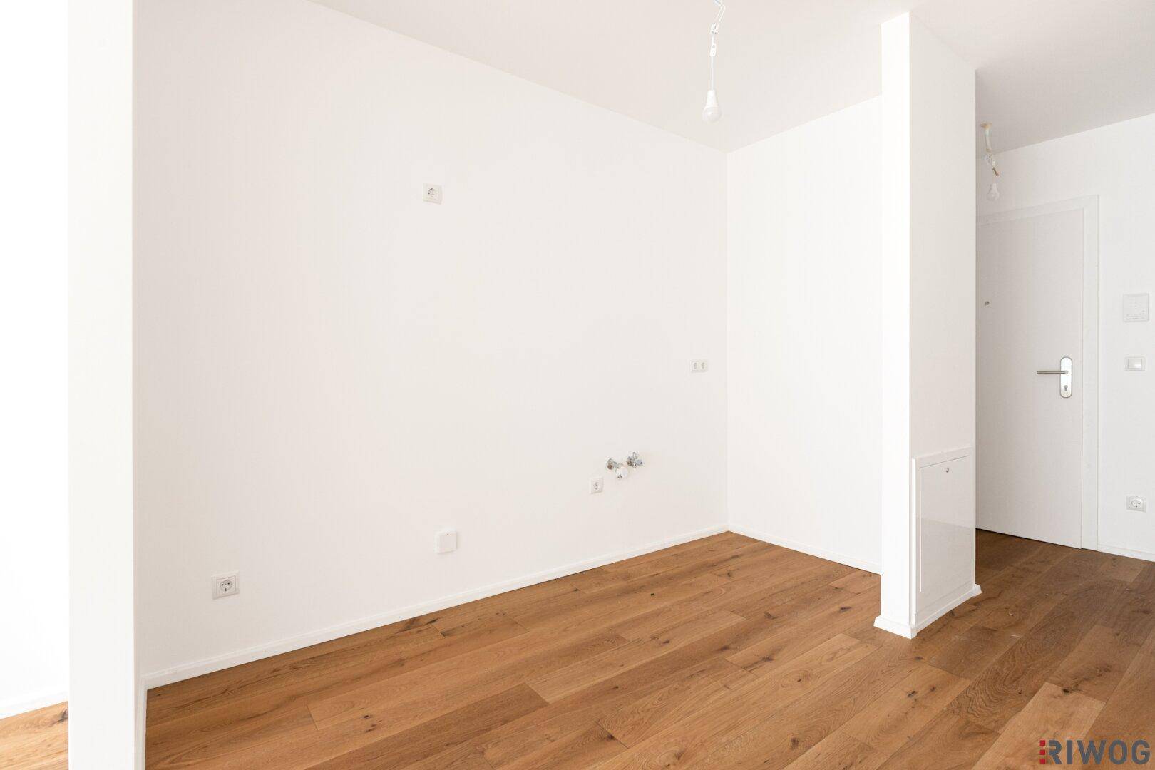 Ecke eines Raumes mit Anschlüssen für eine Küche, ausgestattet mit weiß gestrichenen Wänden und Holzboden.