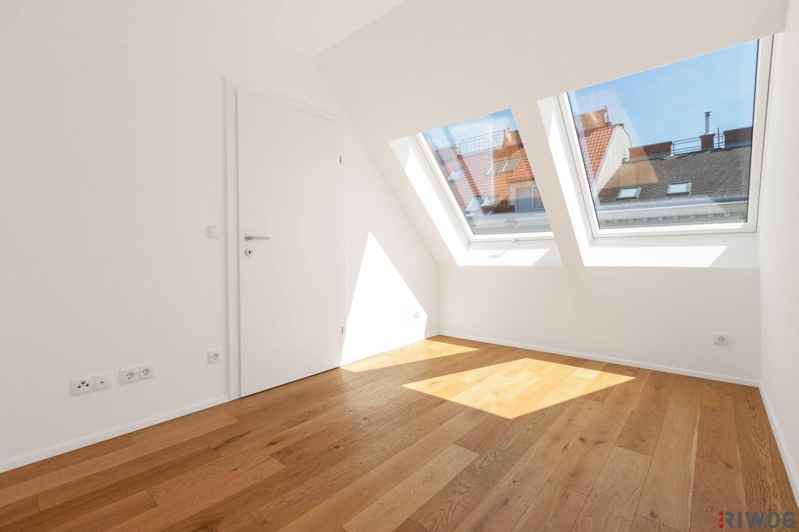 Heller Wohnbereich mit Holzboden und zwei Dachfenstern, die den Raum mit natürlichem Licht durchfluten.