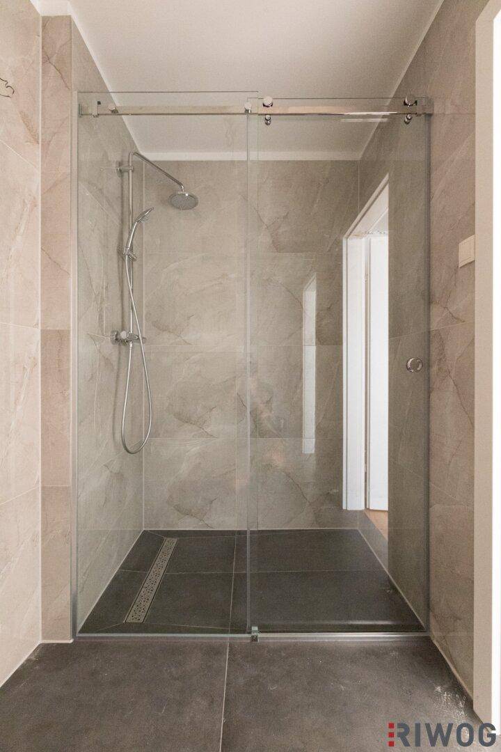 Moderne begehbare Dusche mit Glasabtrennung und eleganten grauen Fliesen im Badezimmer.