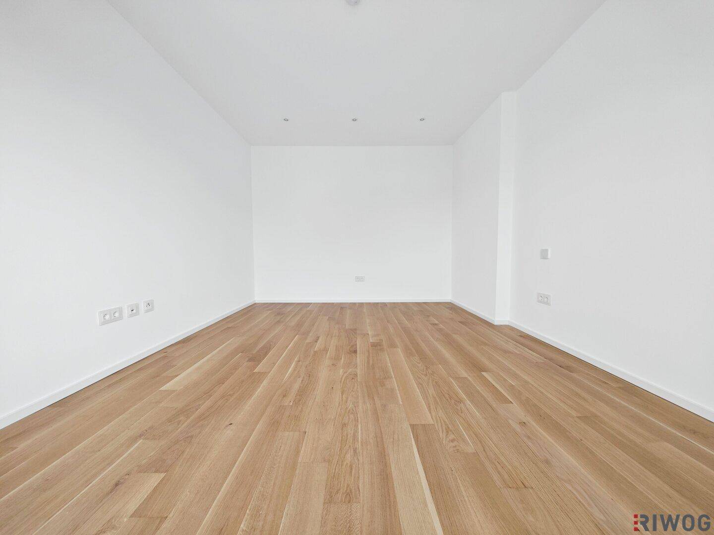 Leeres Zimmer mit Parkettboden und weißen Wänden, ideal für Schlaf- oder Wohnbereich.