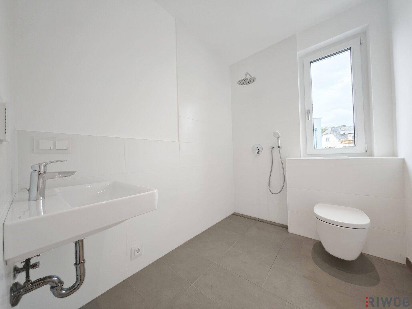 Modernes Badezimmer mit ebenerdiger Dusche, WC und Waschtisch.