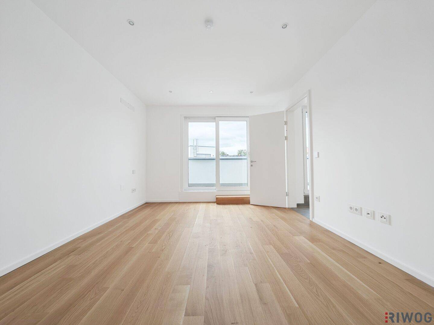 Helles Zimmer mit Parkettboden und Zugang zu einem französischen Balkon.