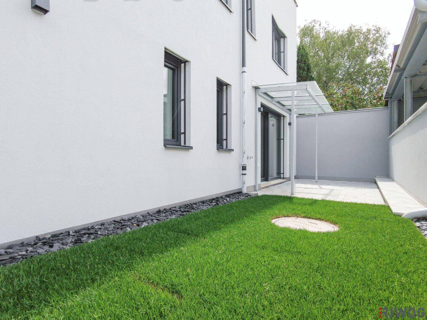 Seitlicher Gartenbereich mit gepflegtem Rasen und dekorativen Steinen entlang der Hauswand.