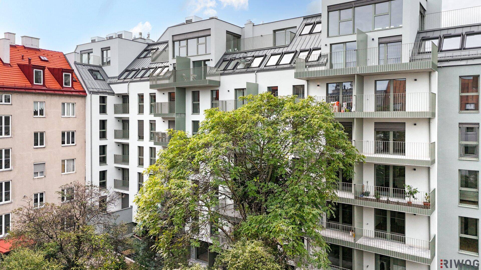 Moderne Wohnfassade mit Balkonen und großen Fenstern, umgeben von grünen Bäumen.