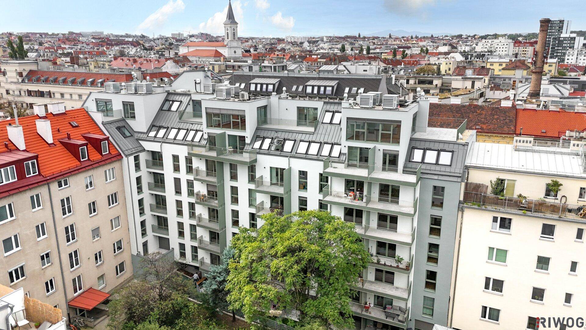 Ansicht eines modernen Wohngebäudes mit mehreren Balkonen und Dachfenstern in städtischer Umgebung.