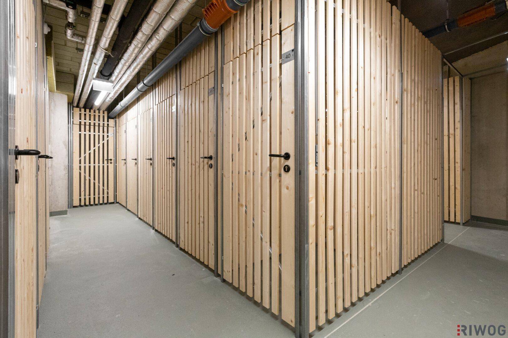 Kellerabteile mit Holzlamellenwänden und Betonboden, gut organisiert für Lagerung.