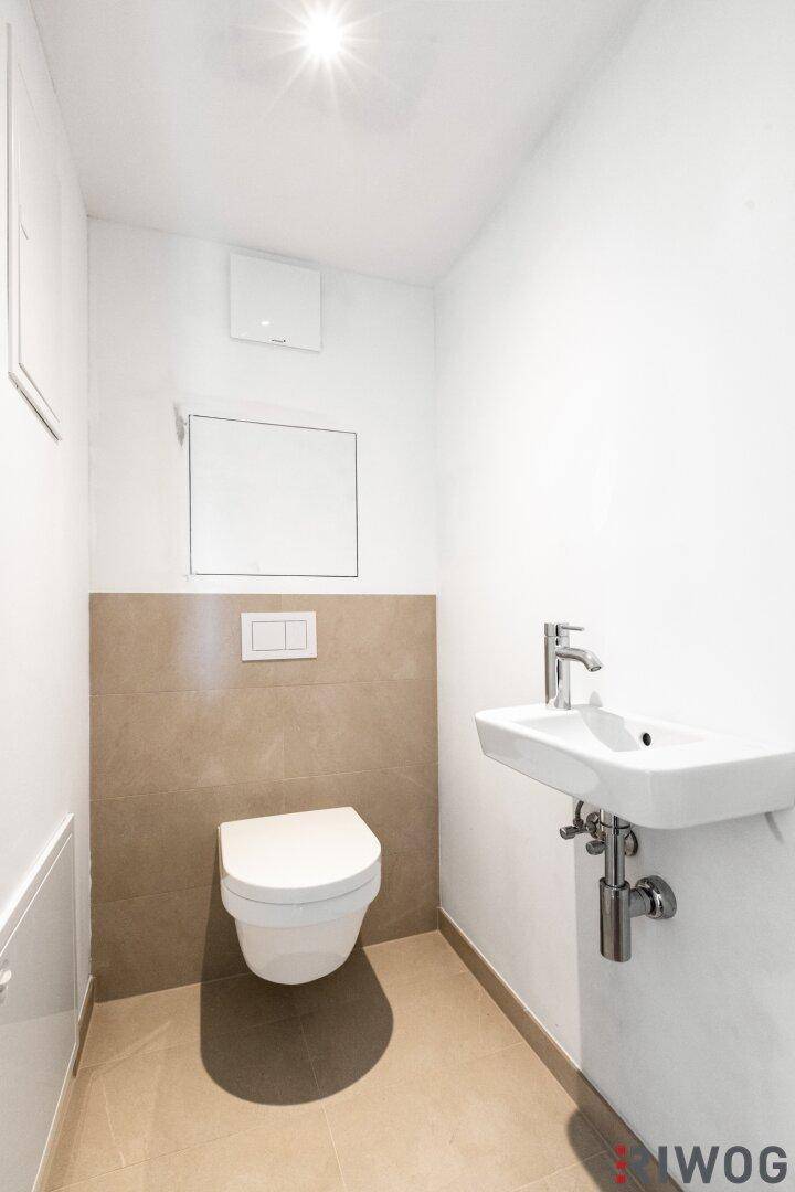 Modernes Gäste-WC mit Wand-WC und kleinem Waschbecken, in hellen Farben gehalten.