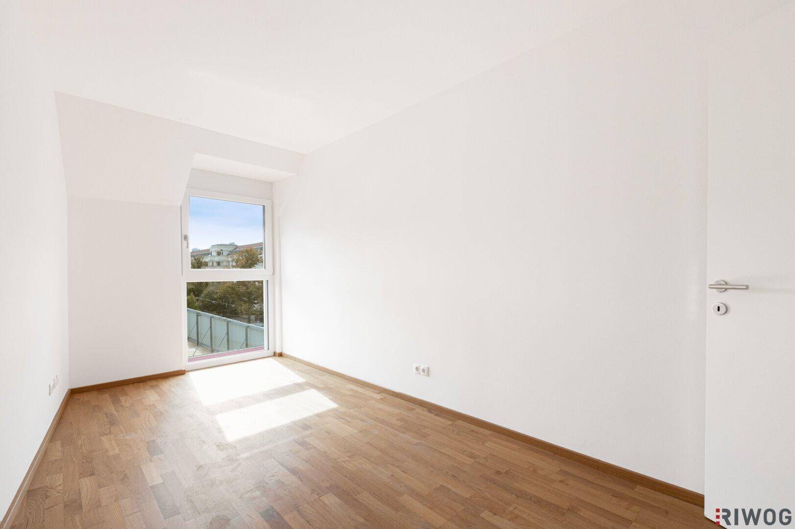 Helles Schlafzimmer mit Parkettboden und großem Fenster für viel Tageslicht, einladend und ruhig.