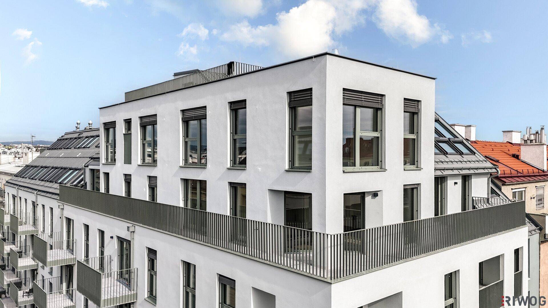 Moderne weiße Gebäudefassade mit großen Fenstern und Balkonen in urbaner Umgebung.