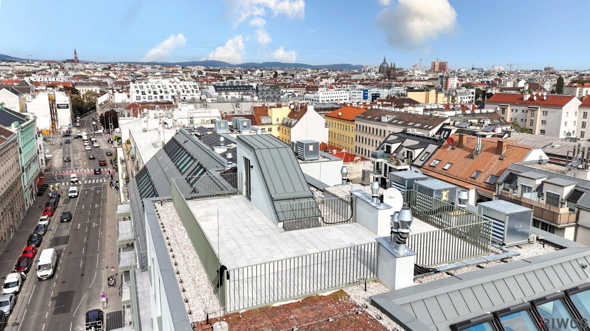 Luftaufnahme eines modernen Wohngebäudes mit Dachterrassen und belebter Straße darunter.