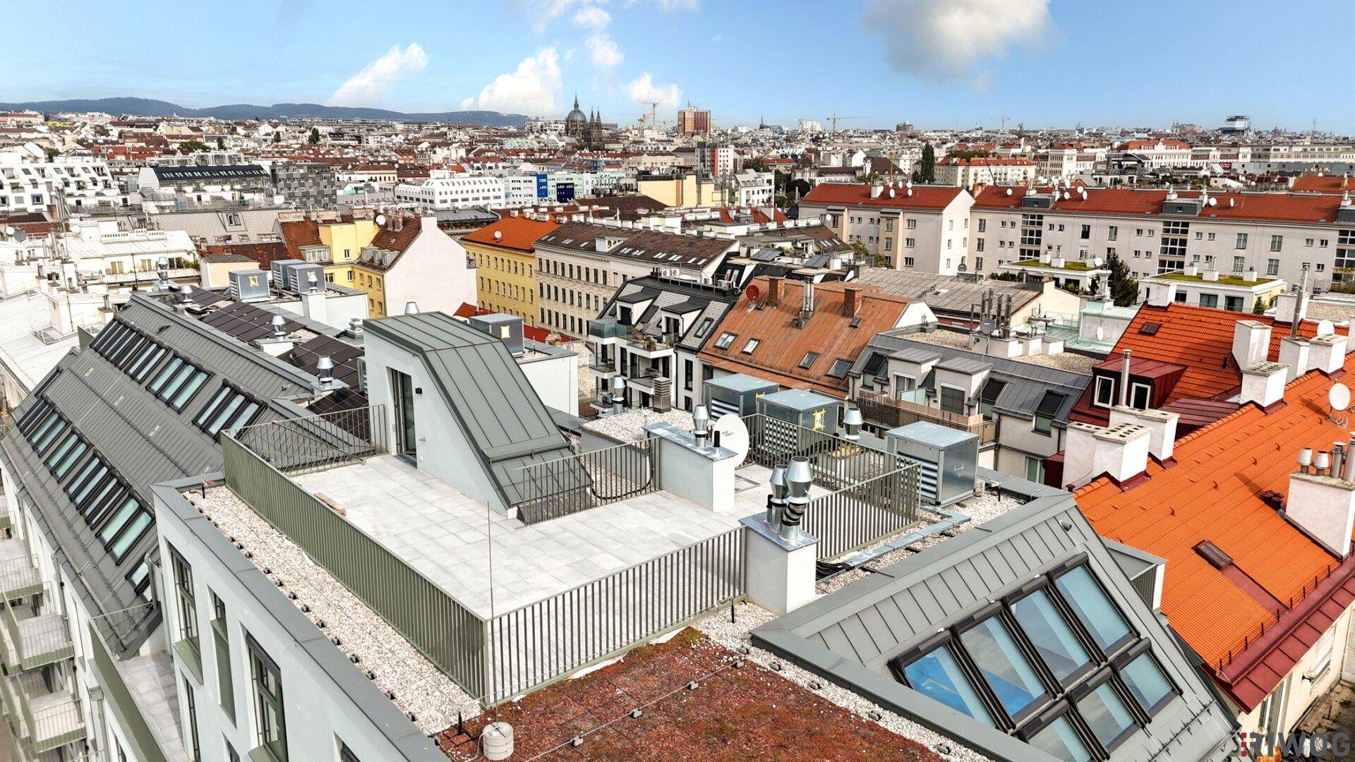 Luftaufnahme eines modernen Gebäudekomplexes mit Dachterrassen und Blick über die Stadt.