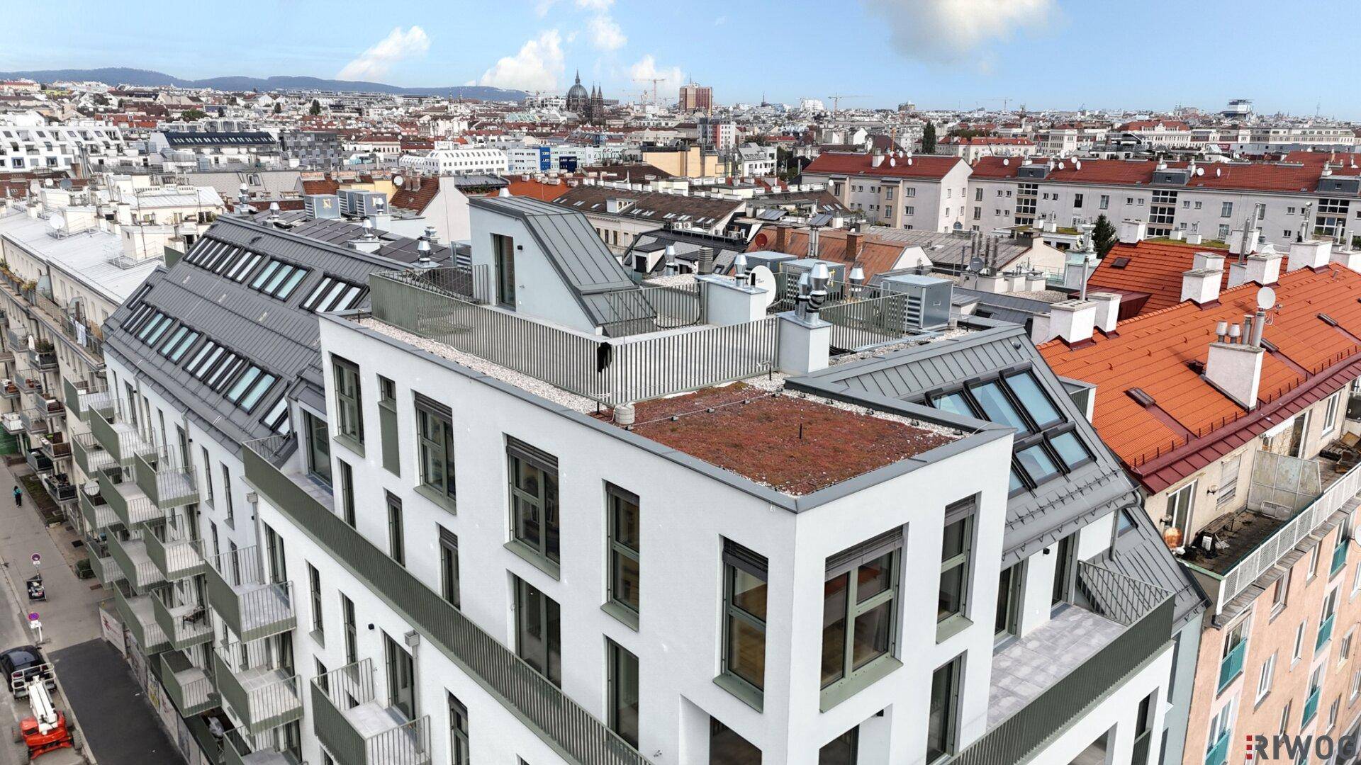 Vogelperspektive eines modernen Wohnkomplexes mit Dachterrassen und umliegenden Gebäuden.