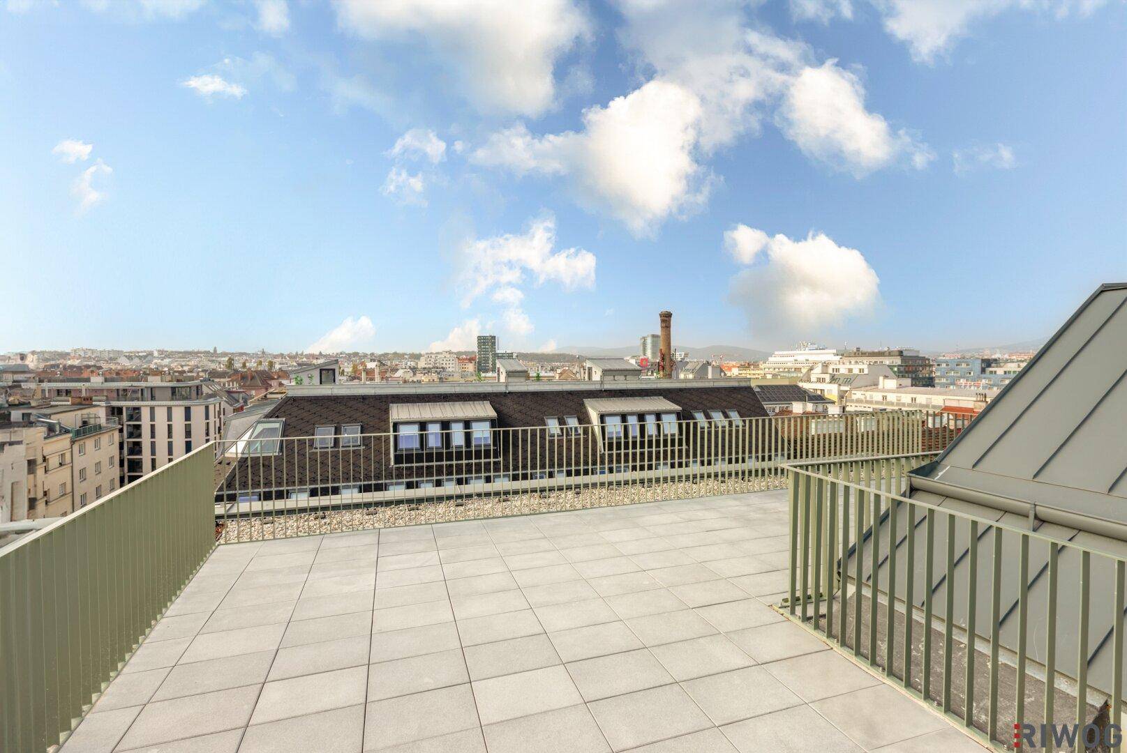 Helle Dachterrasse mit Panoramablick über die Dächer der Stadt und den blauen Himmel.