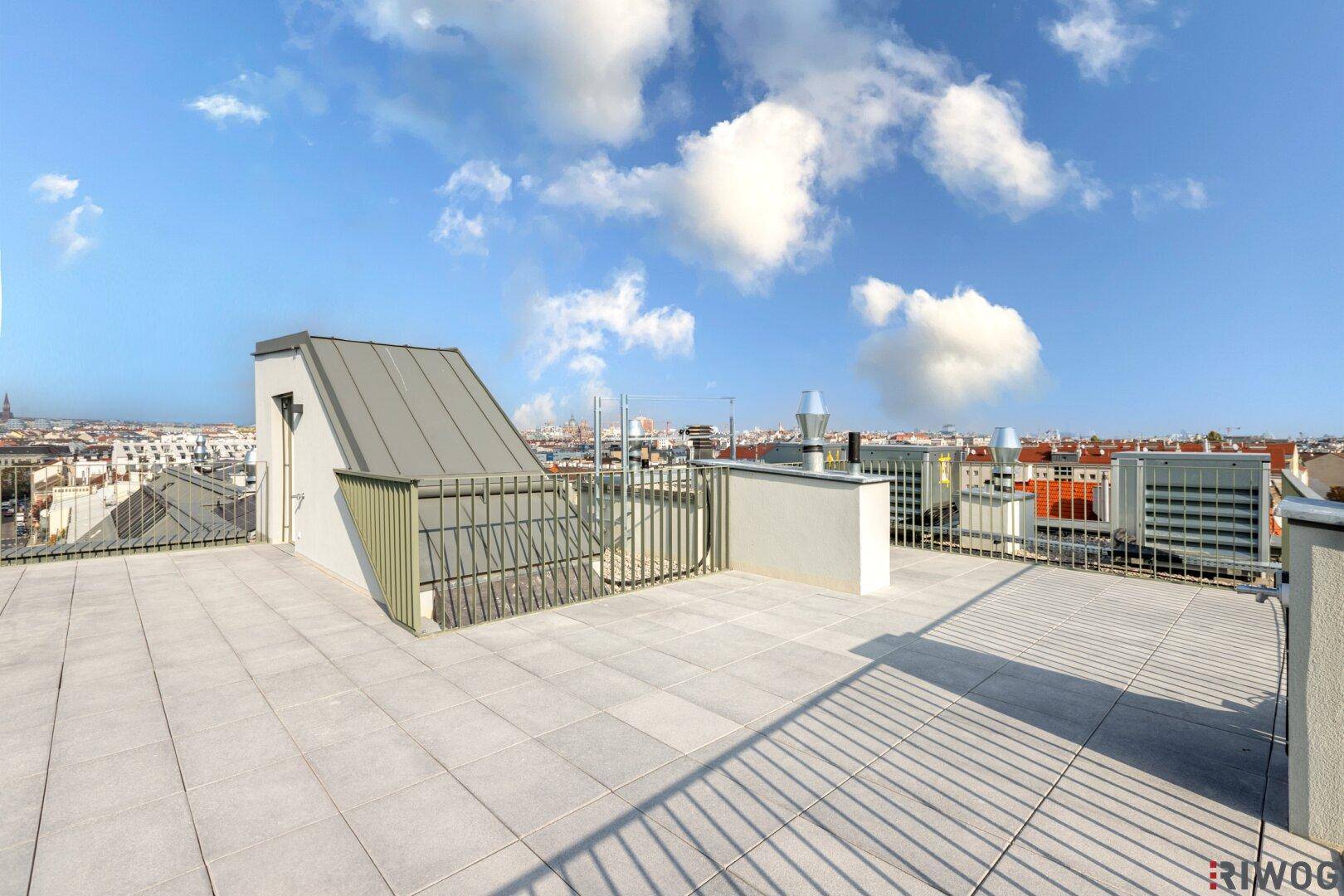 Weitläufige Dachterrasse mit modernem Geländer und sonnigem Ausblick auf die Stadtlandschaft.