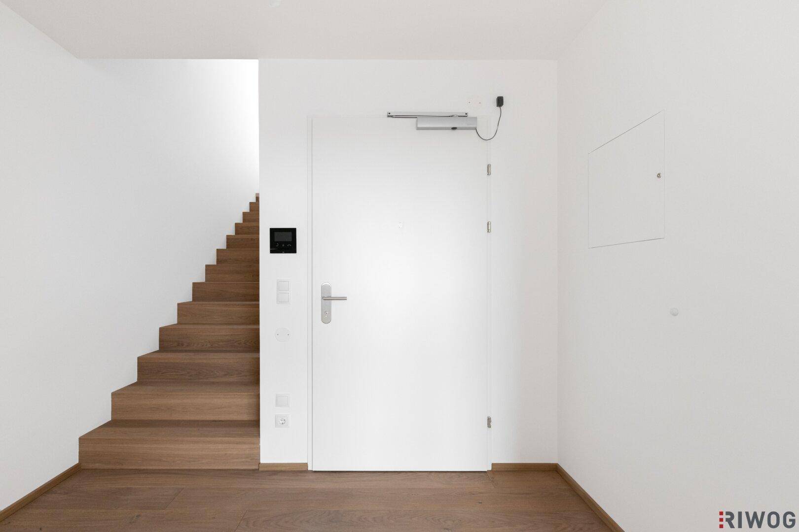 Eingangsbereich mit Holzboden, Treppe und weißer Eingangstür.