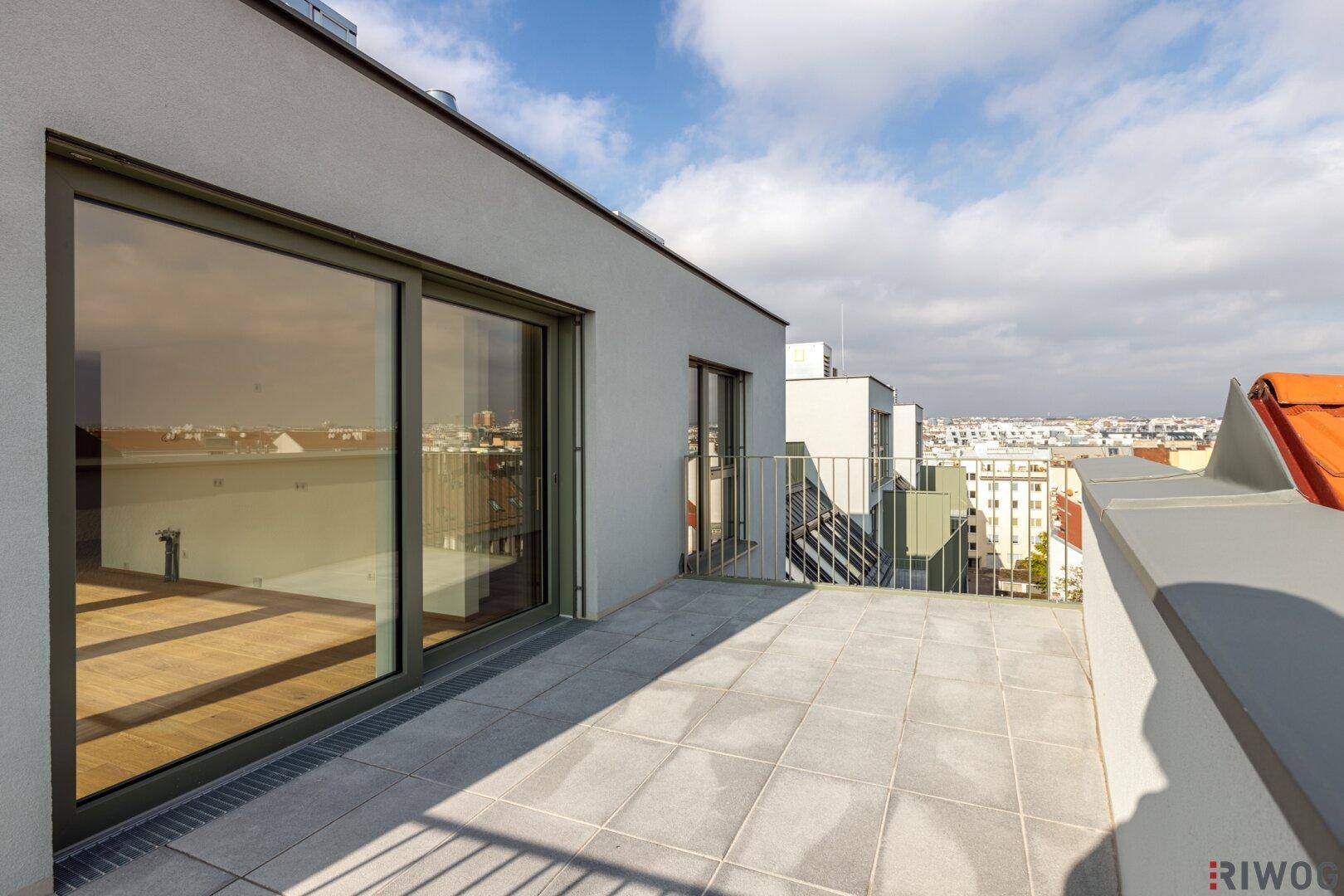Weitläufige Dachterrasse mit Schiebetüren zum Innenbereich und Panoramablick über die Dächer der Stadt.